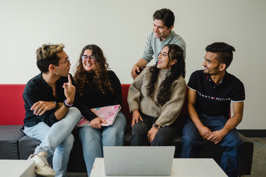 A group of students sit on a couch, talking happily.